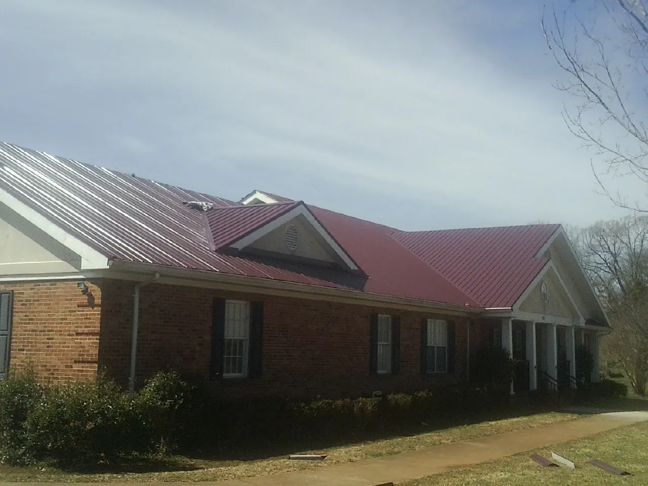 Red metal roof with gabled entries on a long brick building, from a Hail Damage Roof Repair job in Chattanooga